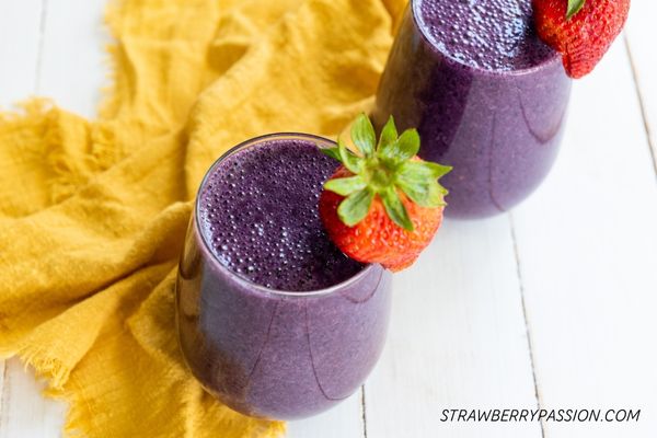 2 vegan berry smoothies in glasses with strawberry garnish on the side of the glass